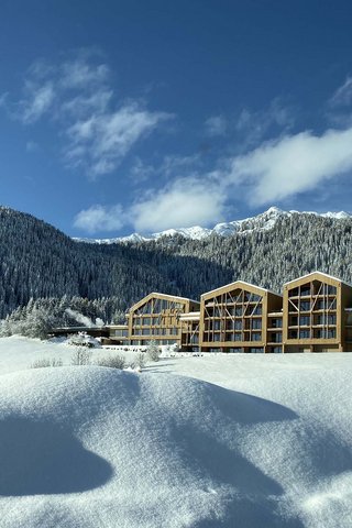 Home Erlebnisort Gassenhof Schneebedecktes Hotel vor bewaldetem Berg unter blauem Himmel