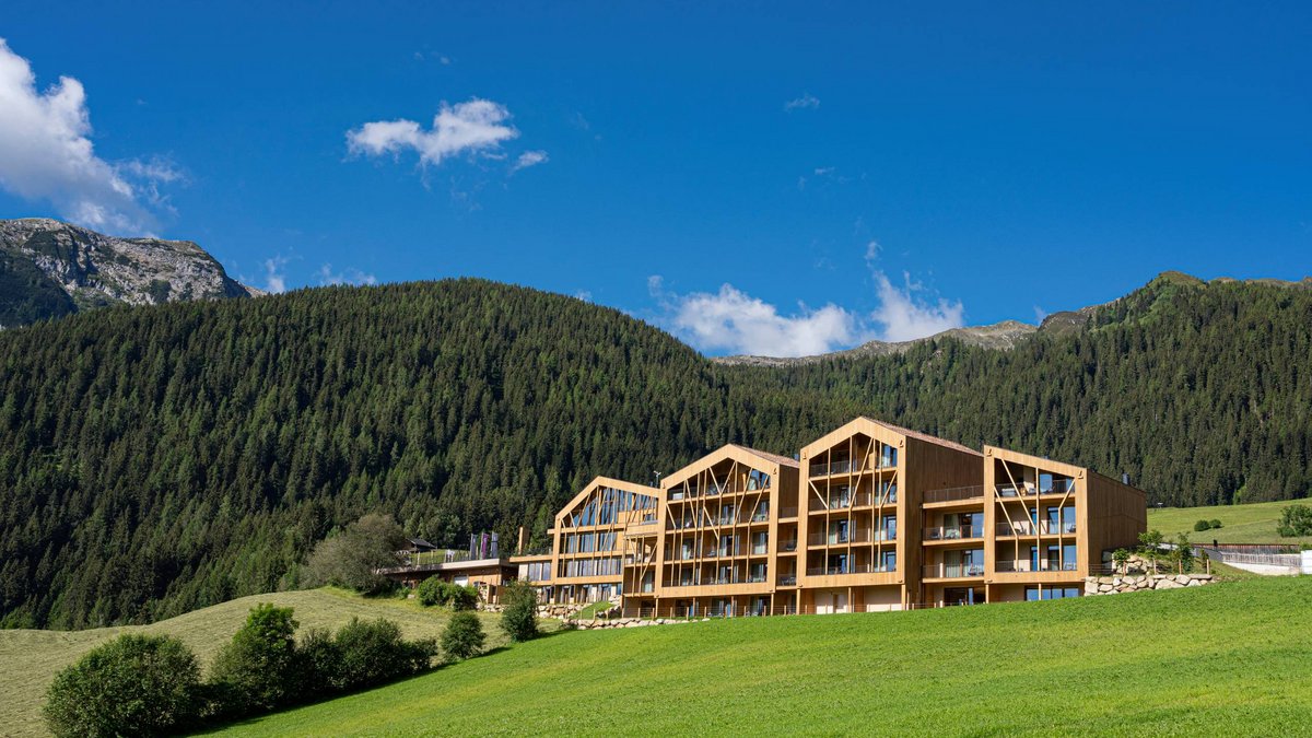 Home Erlebnisort Gassenhof Modernes Holzgebäude vor bewaldetem Berg und blauem Himmel