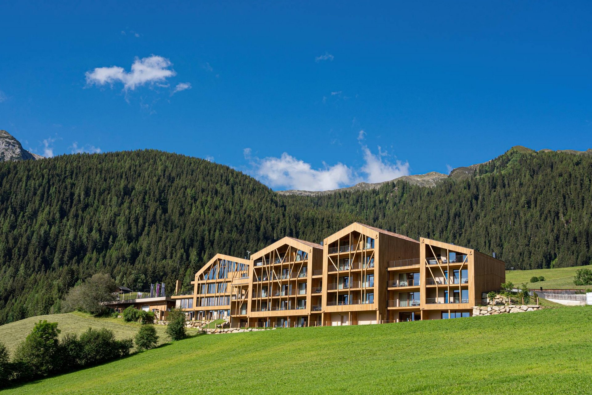 Home Erlebnisort Gassenhof Modernes Holzgebäude vor bewaldetem Berg und blauem Himmel