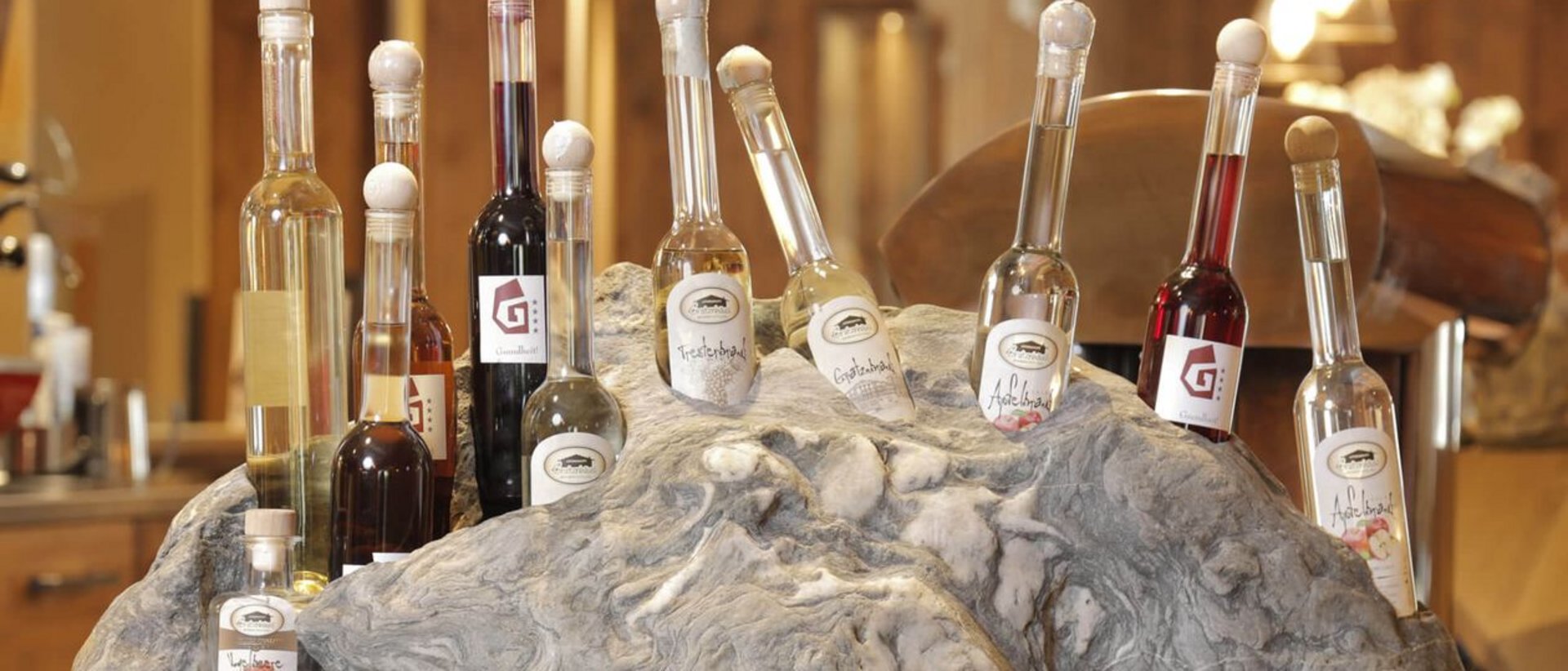 Home Erlebnisort Gassenhof Verschiedene Schnapsflaschen in einem großen Steinhalter in warmer Umgebung