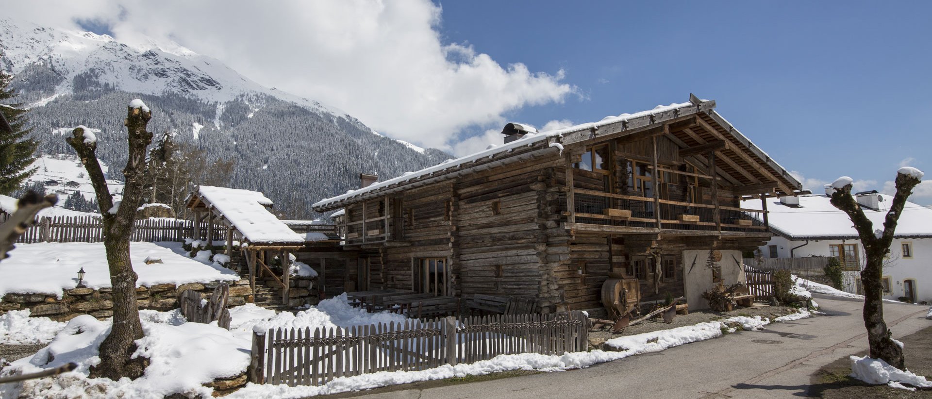 Home Erlebnisort Gassenhof Altes Holzhaus im Schnee mit Bergpanorama unter blauem Himmel