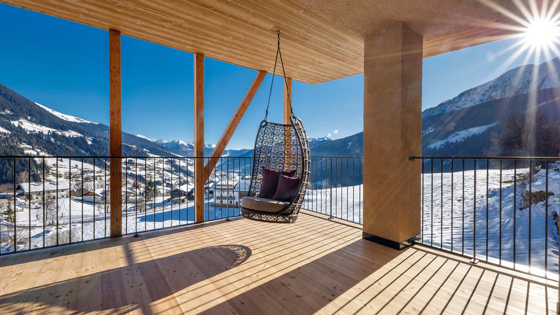 Home Erlebnisort Gassenhof Hängesessel auf Balkon mit Blick auf schneebedeckte Berge und sonnigen Himmel