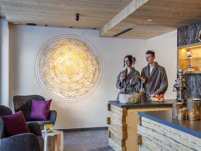 Home Erlebnisort Gassenhof Paar in Bademänteln steht in modernem Spa-Bereich mit Holz und gemütlichen Sesseln