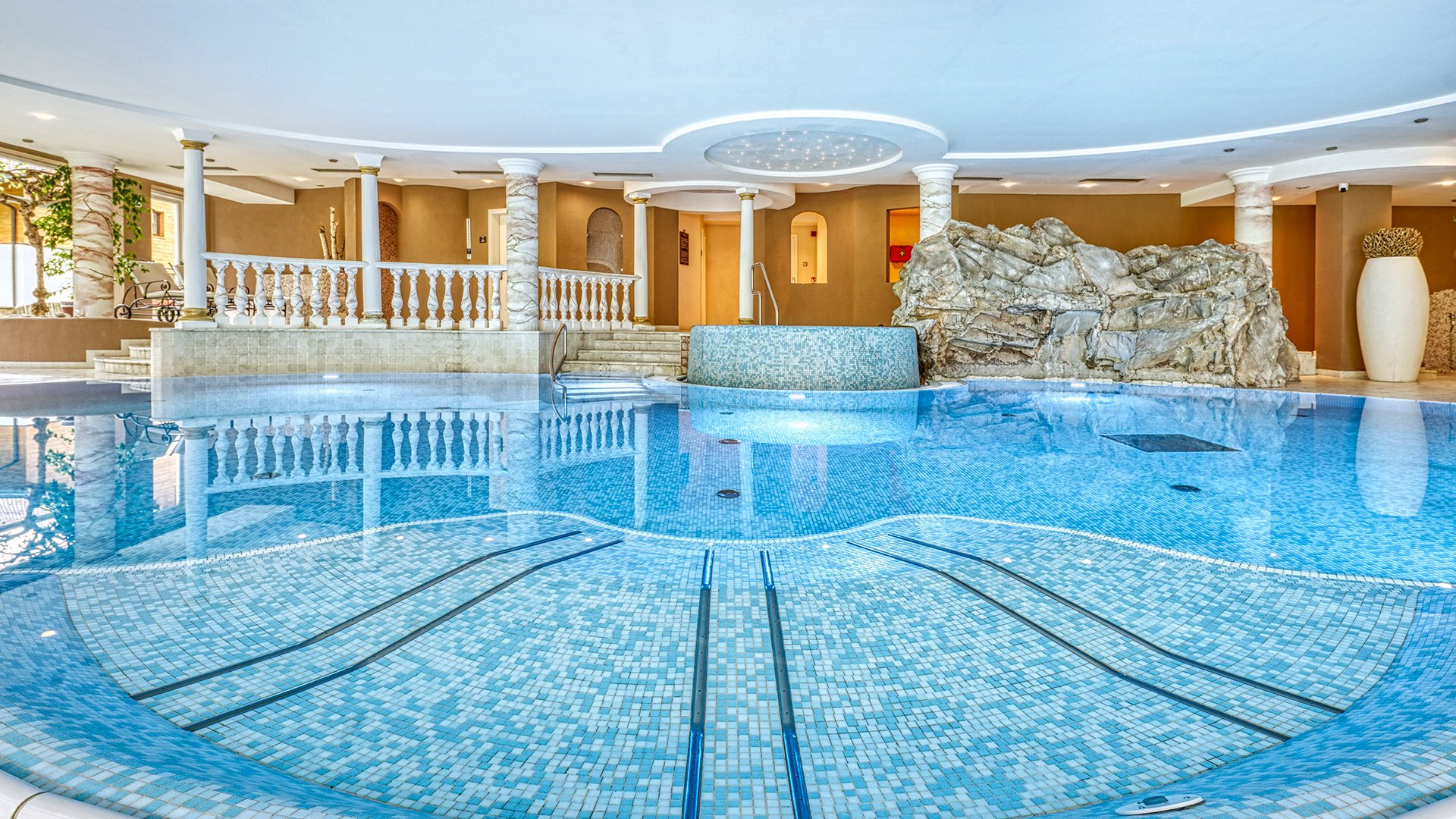 Home Erlebnisort Gassenhof Innenansicht eines luxuriösen Schwimmbads mit Mosaikfliesen und Säulen
