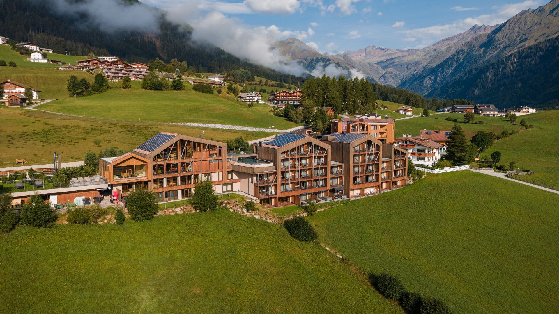 Home Erlebnisort Gassenhof Alpenhotel in grüner Berglandschaft mit bewaldeten Hängen und Bergen im Hintergrund