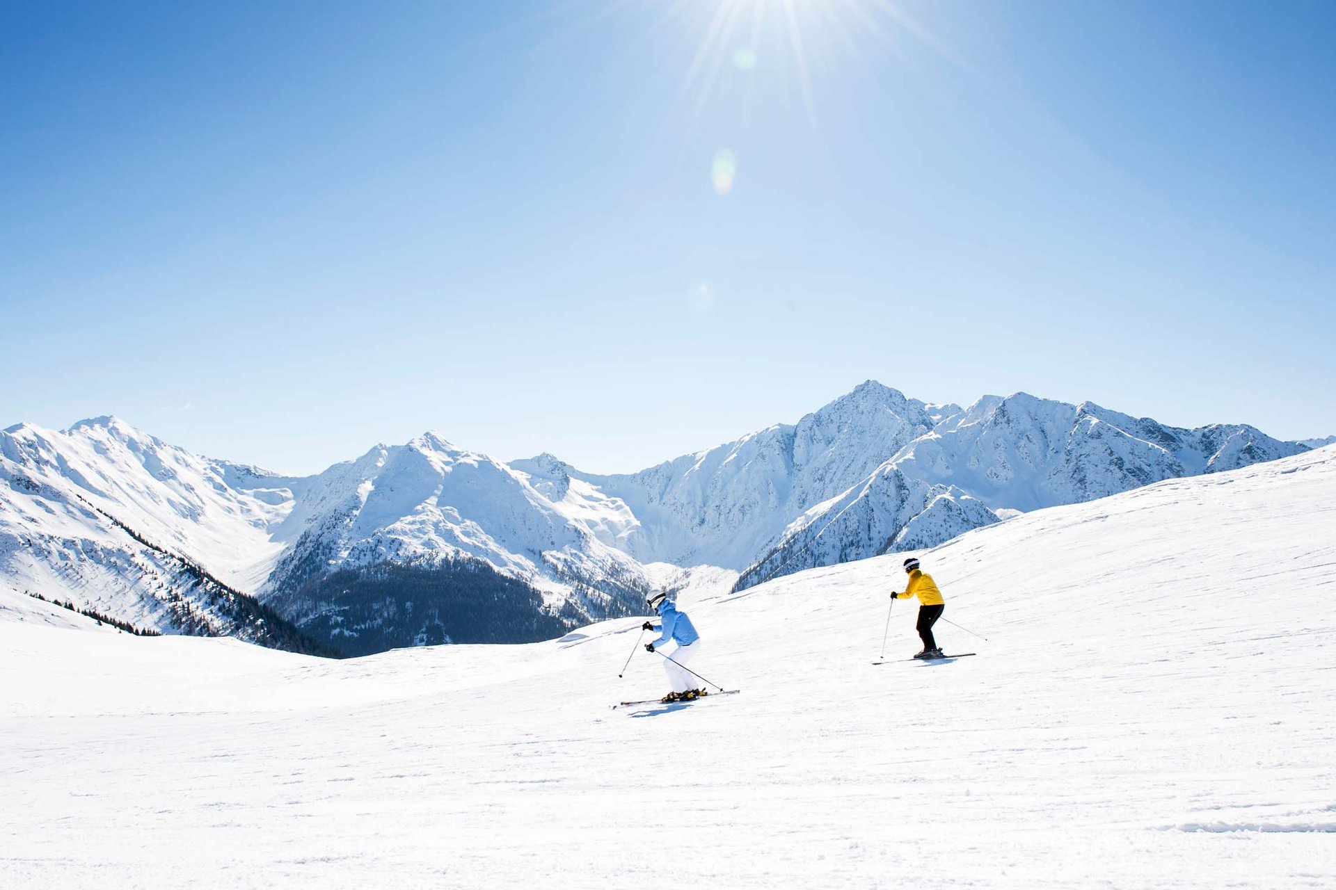 Home Erlebnisort Gassenhof Zwei Skifahrer auf verschneiter Piste mit Bergen bei klarem Himmel