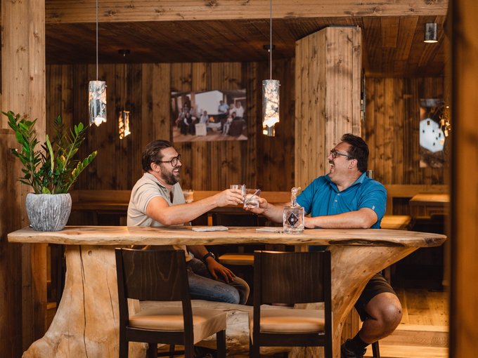 The Volgger family Two men clinking glasses at a rustic wooden table in a wood-paneled room