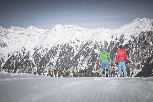 Your holiday in South Tyrol Two people walking on snowy trail with snow-covered mountains in background