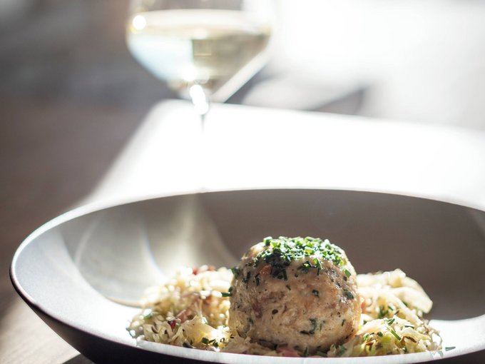 Your holiday in South Tyrol Herb dumpling on a plate with a glass of white wine in the background