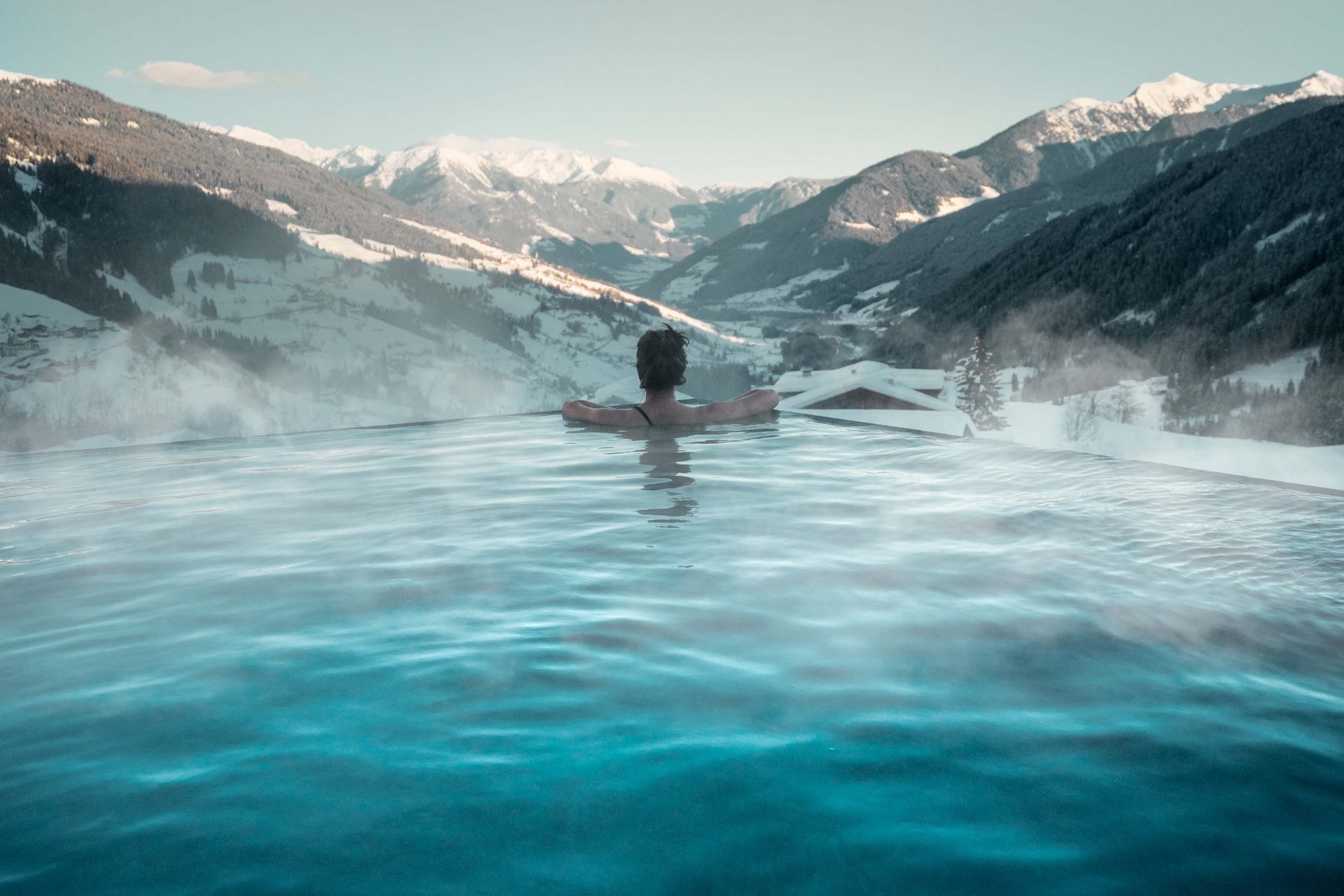 Home Erlebnisort Gassenhof Person im Außenpool mit Blick auf schneebedeckte Berge