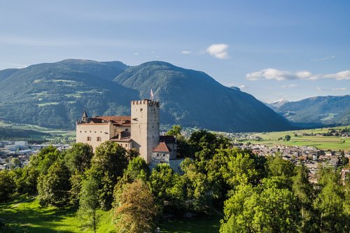Your holiday in South Tyrol Castle on wooded hill with mountains and town in the background