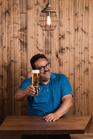 Home Erlebnisort Gassenhof Mann in blauem Hemd hält ein Bierglas in rustikalem Holzinterieur