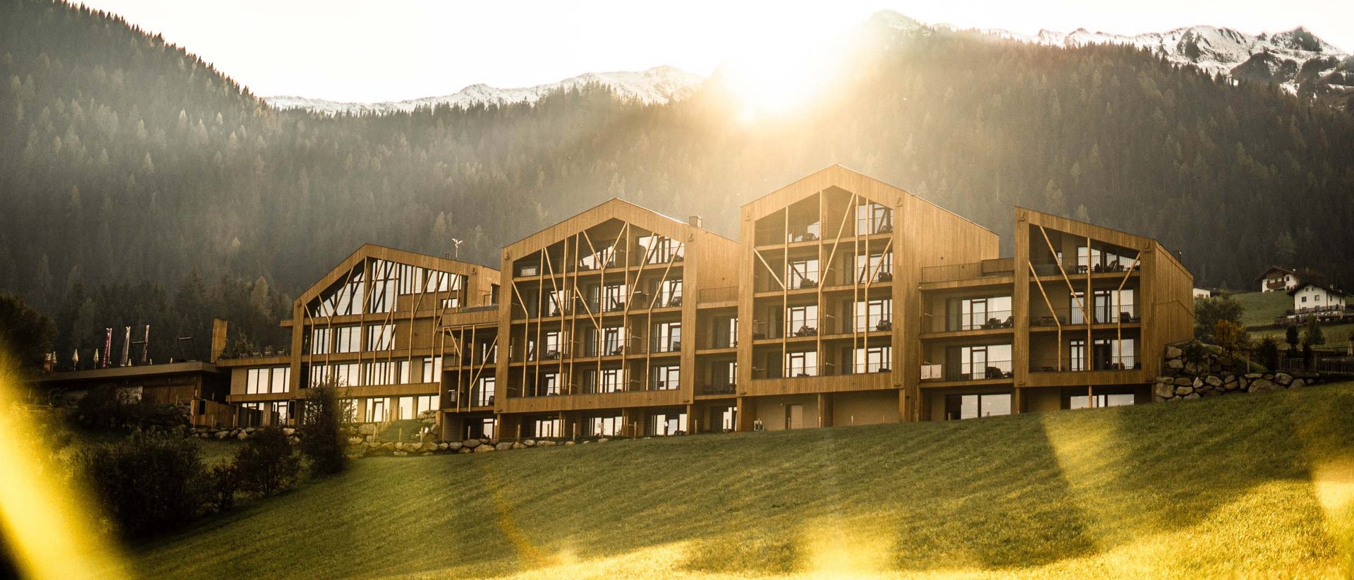 Home Erlebnisort Gassenhof Modernes Holzgebäude vor bewaldeten Bergen im Sonnenlicht