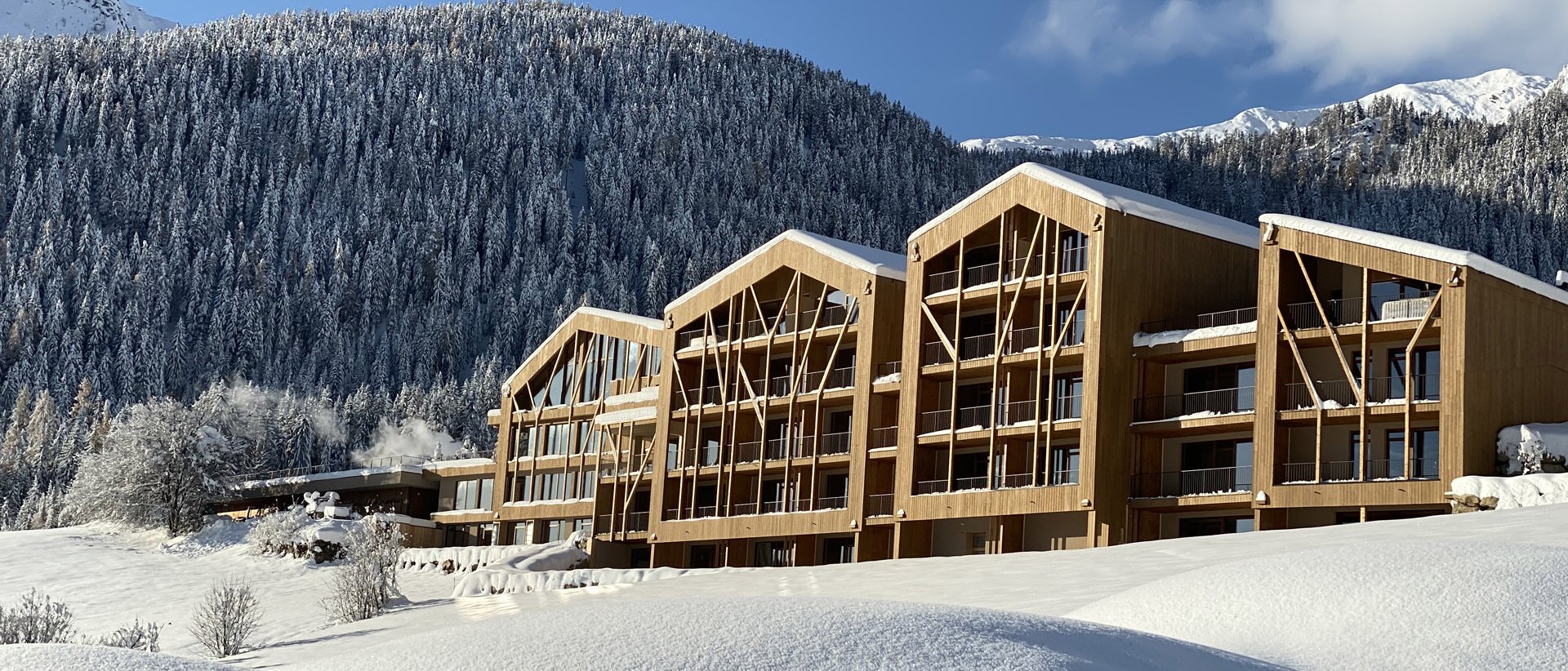 Home Erlebnisort Gassenhof Moderne Holzhäuser im verschneiten Bergland unter blauem Himmel