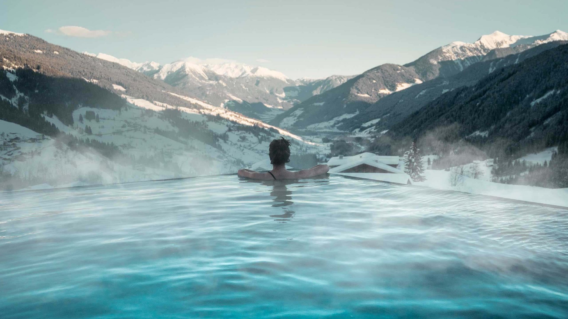 Home Erlebnisort Gassenhof Person entspannt im beheizten Pool mit Blick auf schneebedeckte Berge
