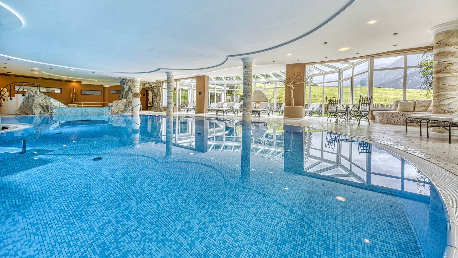 Home Erlebnisort Gassenhof Großes Hallenbad mit blauen Fliesen und Lounge-Bereich mit Aussicht auf Berge