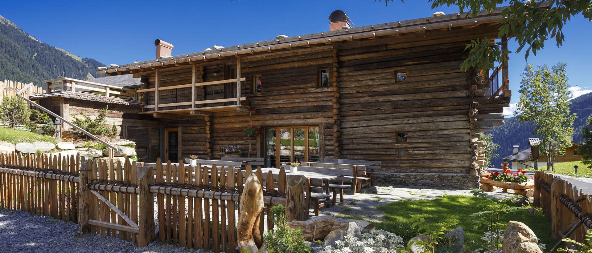 Home Erlebnisort Gassenhof Rustikales Holzhaus mit Garten und Bergblick bei klarem Himmel