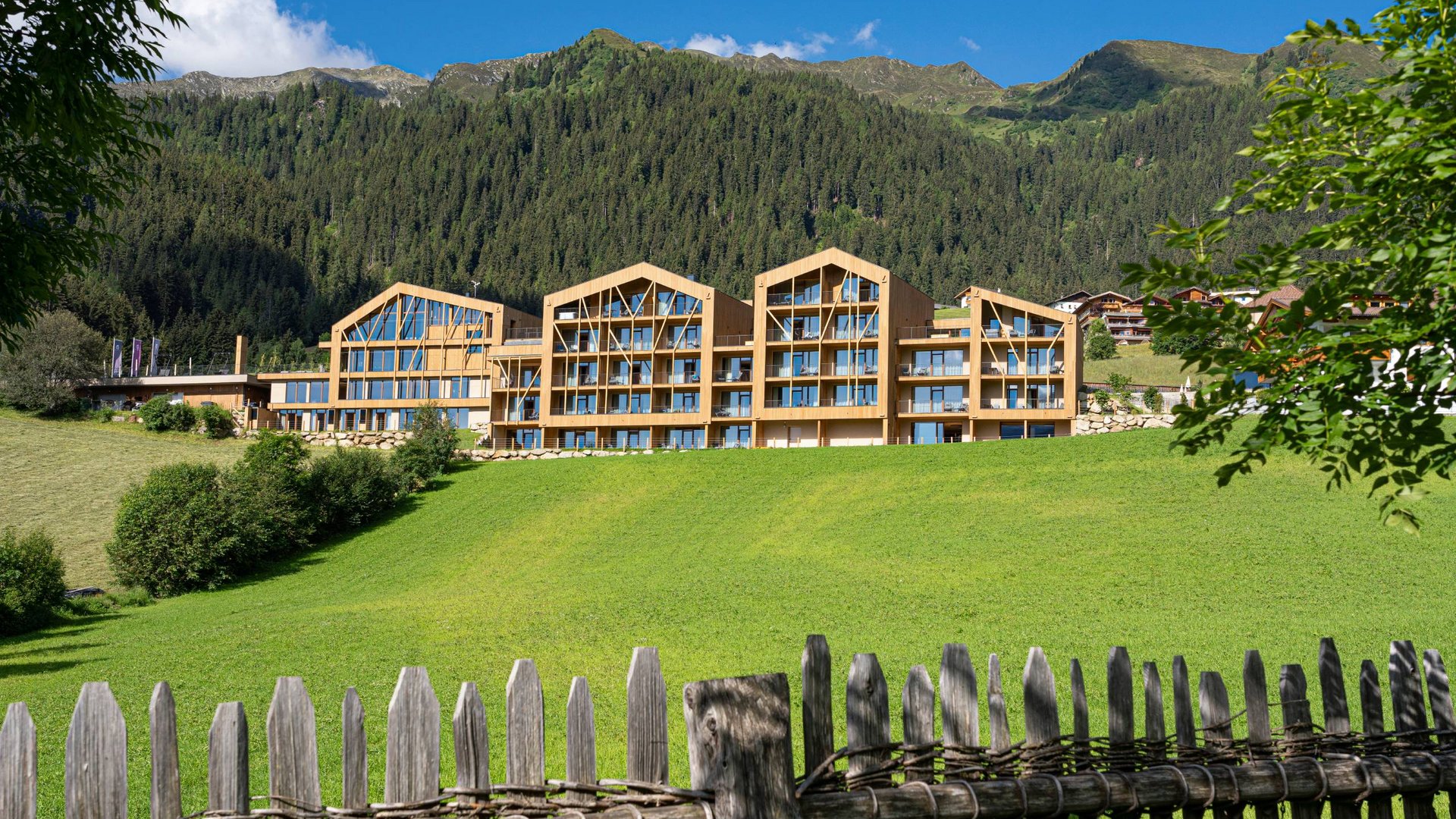 Home Erlebnisort Gassenhof Moderner Holzbau-Komplex vor bewaldeten Bergen und grünem Wiesenhang